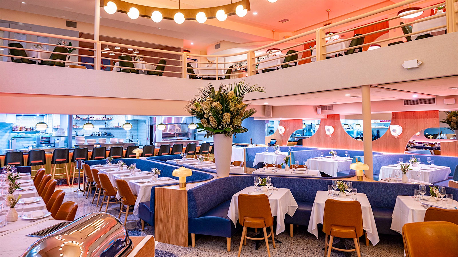     Una sala da pranzo Monterey a più livelli con divanetti blu brillante e sedie marroni al primo piano e una cucina aperta lungo la parete di fondo
